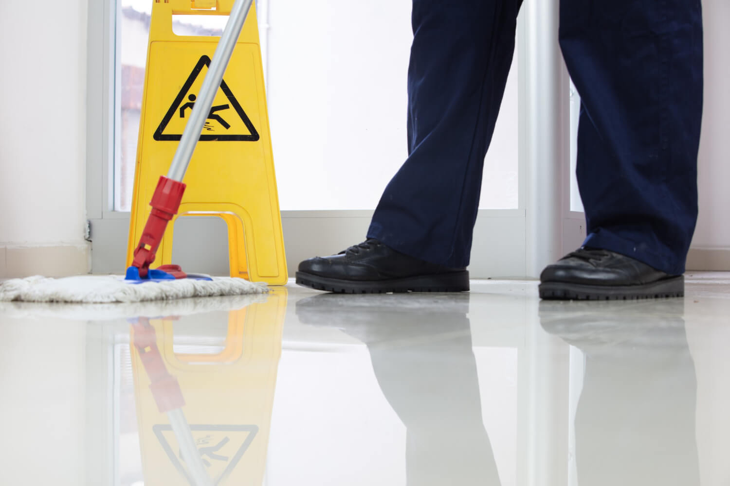 janitor mopping floor in front of a wet floor sign