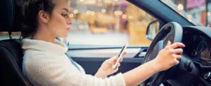 young woman looking at her phone while driving distracted driving in Suburban Maryland